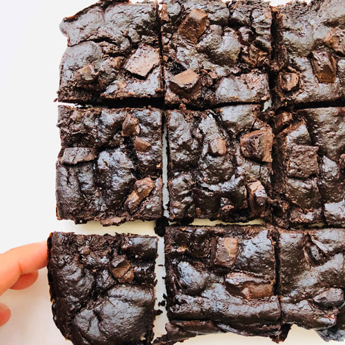 A person taking a piece of chocolate chip brownie, from an already cut brownie