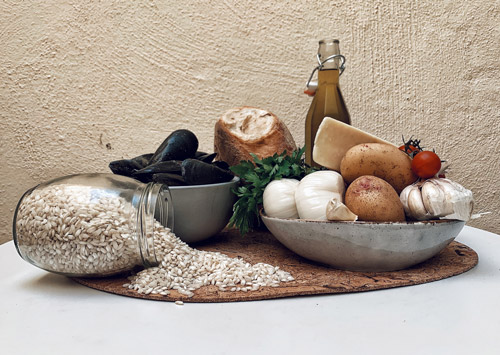 An assortment of rice, garlic, onions, tomatoes, potatoes, oil, mussels, parsley and bread all beautifully set up