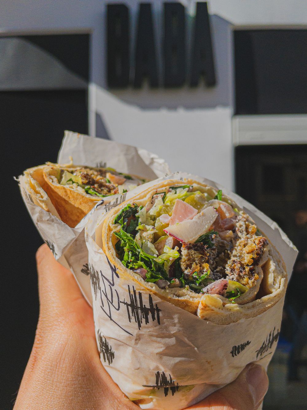 A BABA Sandweesh filled with the freshest of ingredients, BABA restaurant in the bakground.